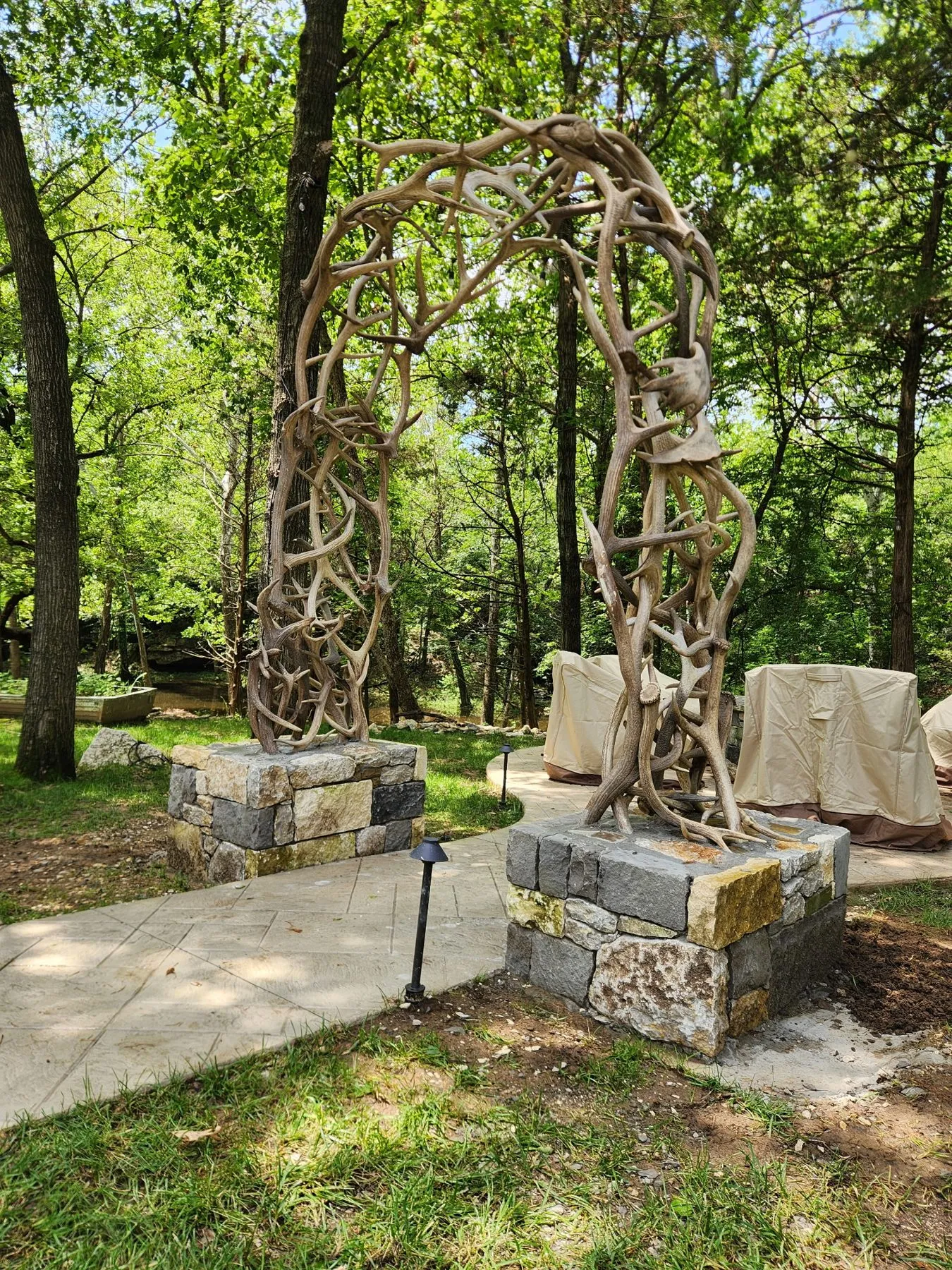 Real elk antler arch over a stone path to a fire pit with stone columns at both bases in Owasso