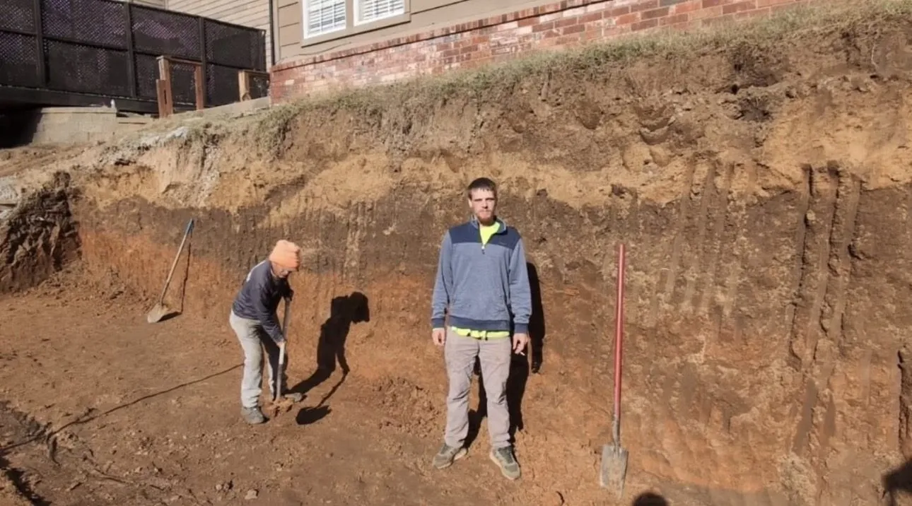 Crew excavating beside a Broken Arrow house for an engineered 11-foot retaining wall with a French drain