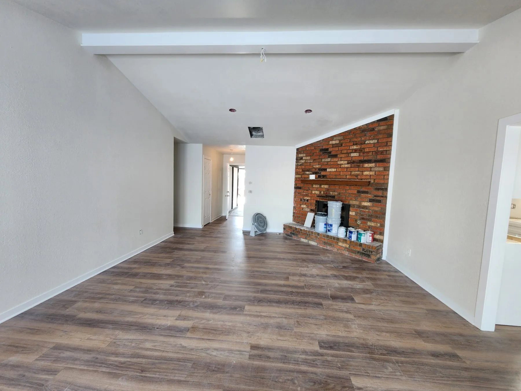 Open living area with wood-look flooring, freshly painted white walls and a brick fireplace after a Tulsa interior repaint