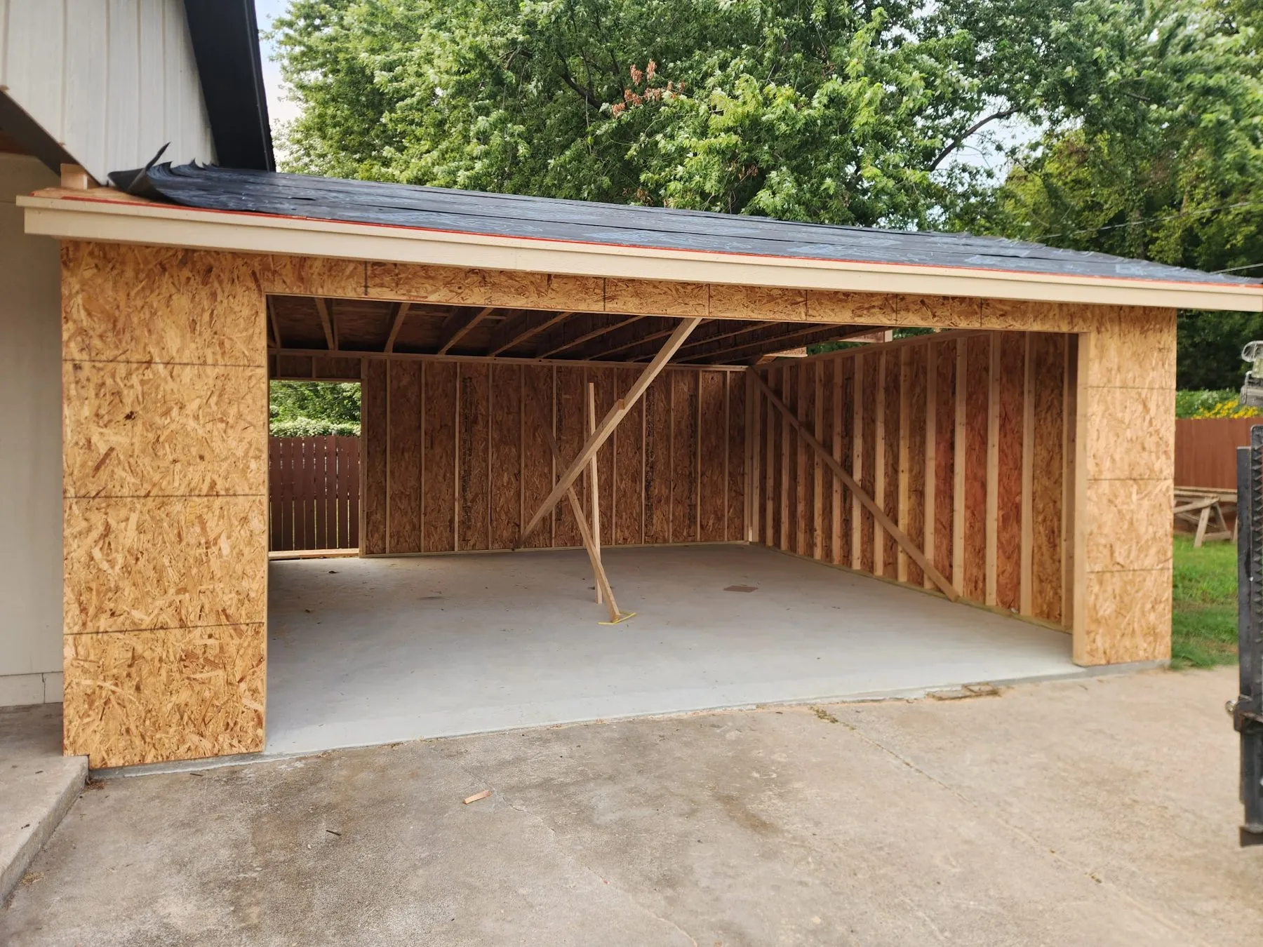 Wall framing and roof trusses on the concrete slab of a detached garage built from the ground up in Broken Arrow