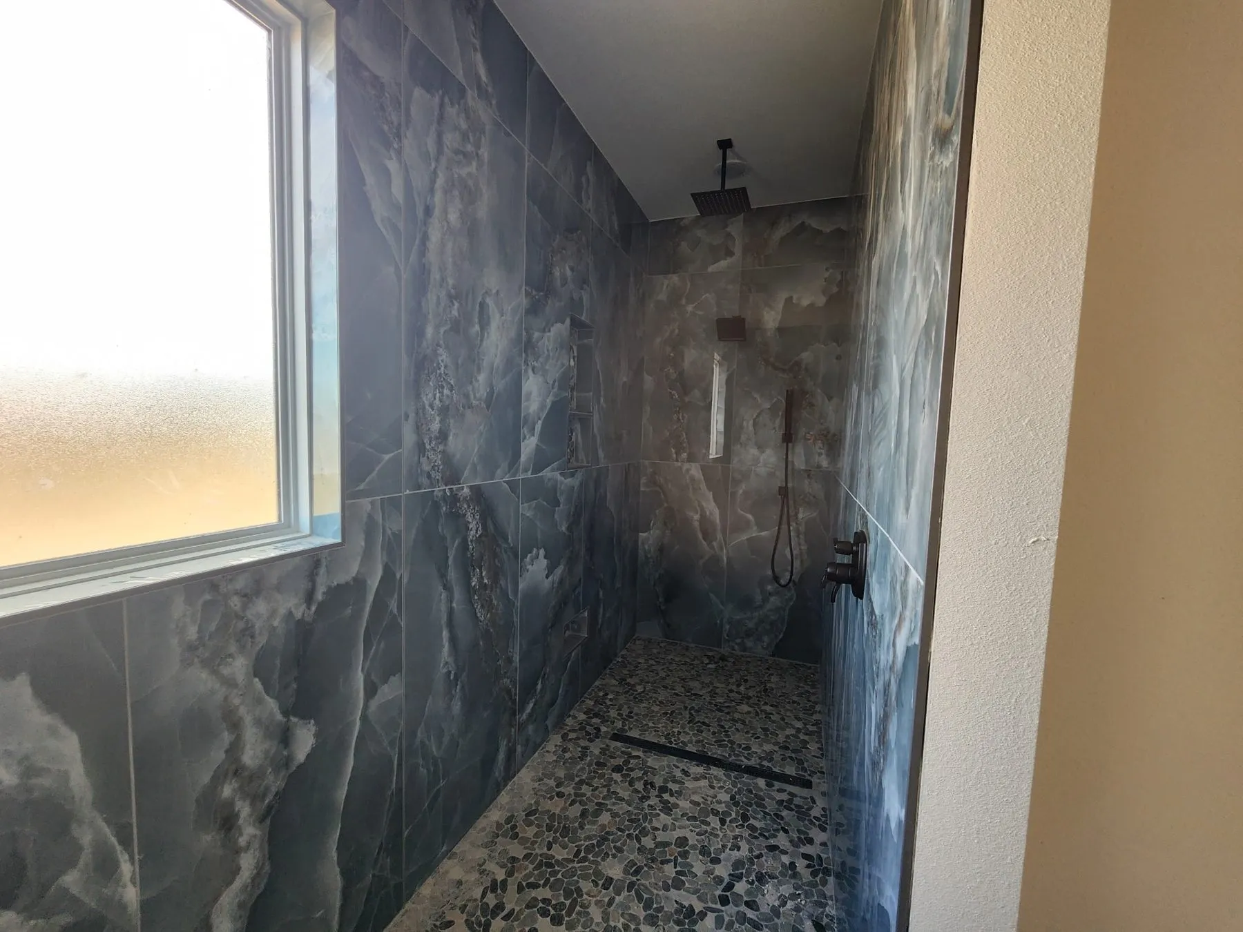 New walk-in tile shower with large-format wall tile and a pebble floor in a Broken Arrow bathroom