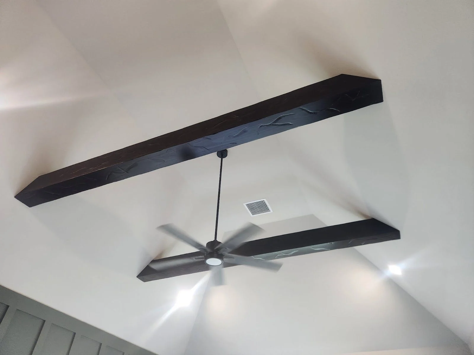 Dark wood ceiling beams built and installed above a ceiling fan in a repainted Bixby room